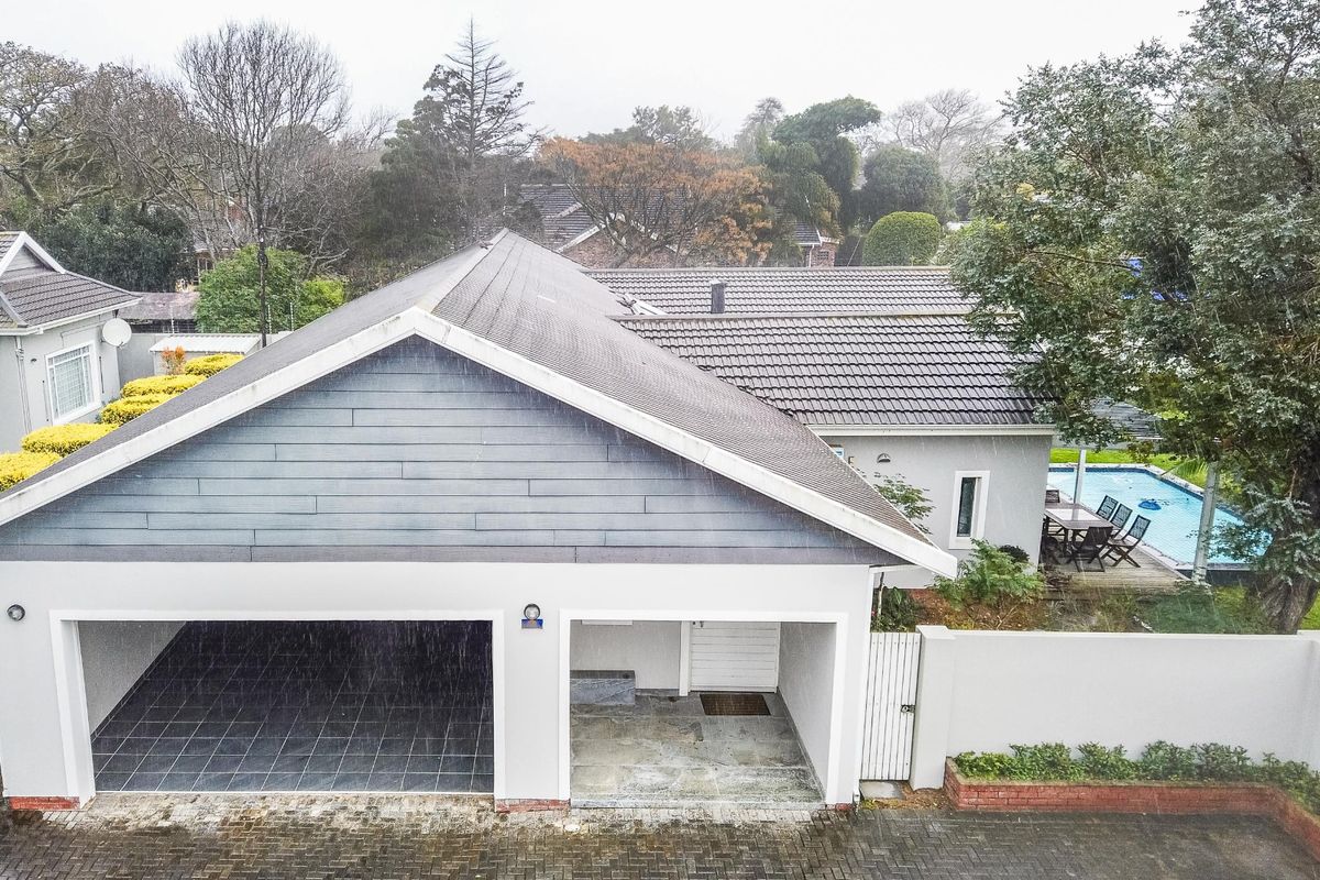 Aerial view of the property featuring a tiled roof, double garage, paved driveway, and a swimming pool in the rear garden area.
