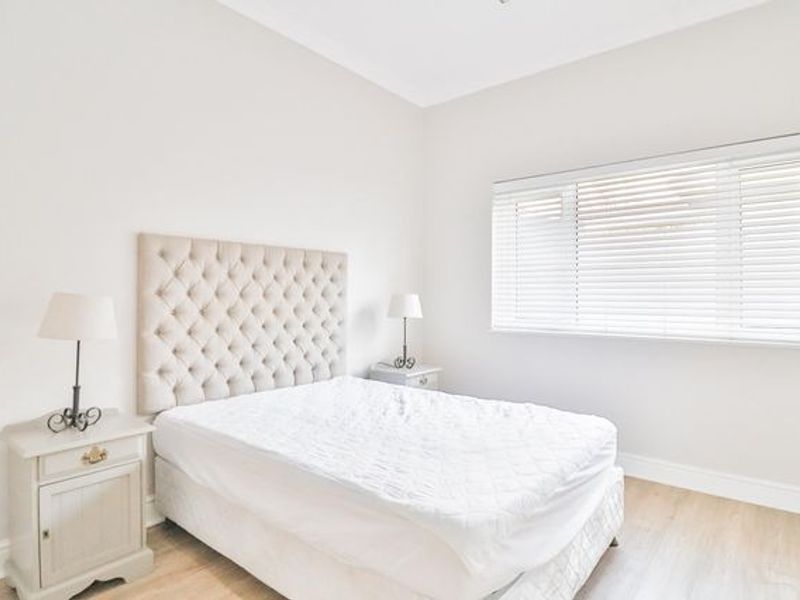 A bright and neutral bedroom featuring light wood-look flooring, coving, and fitted venetian blinds.