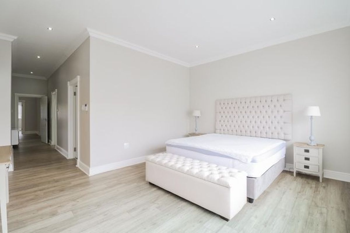 Spacious bedroom featuring light-toned laminate flooring, recessed downlighting, and elegant crown molding, creating a bright and neutral living space.