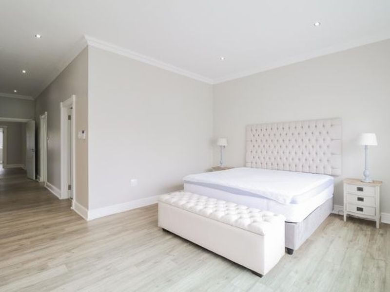 Spacious bedroom featuring light-toned laminate flooring, recessed downlighting, and elegant crown molding, creating a bright and neutral living space.