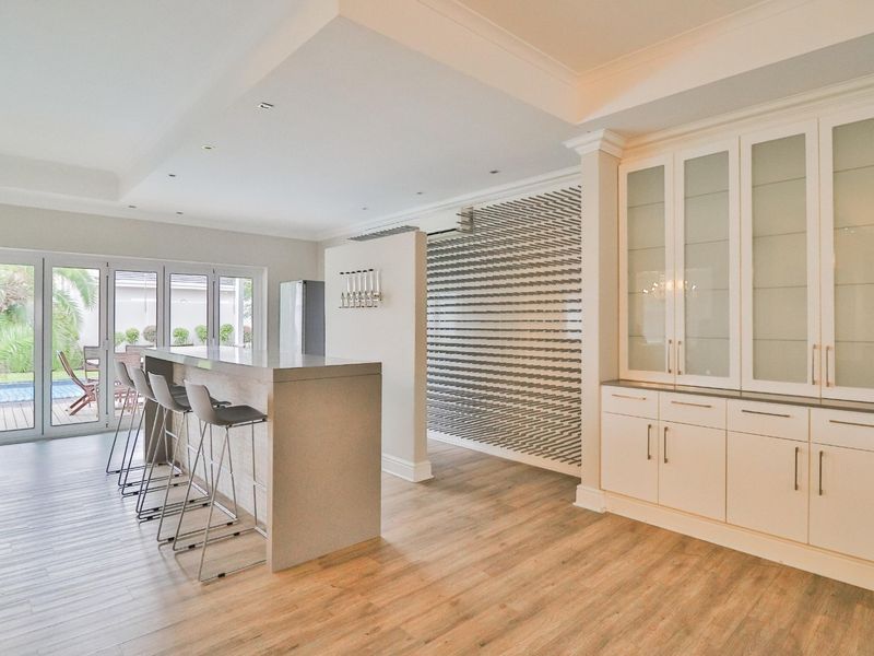 Spacious open-plan living area featuring a modern breakfast bar, custom built-in cabinetry, and seamless access to the outdoor patio through glass french doors.