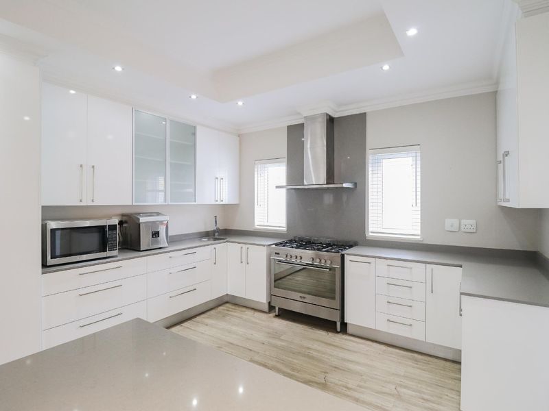 Modern kitchen featuring white cabinetry, stone countertops, stainless steel gas stove, extractor fan, and recessed lighting with a clean, contemporary finish.