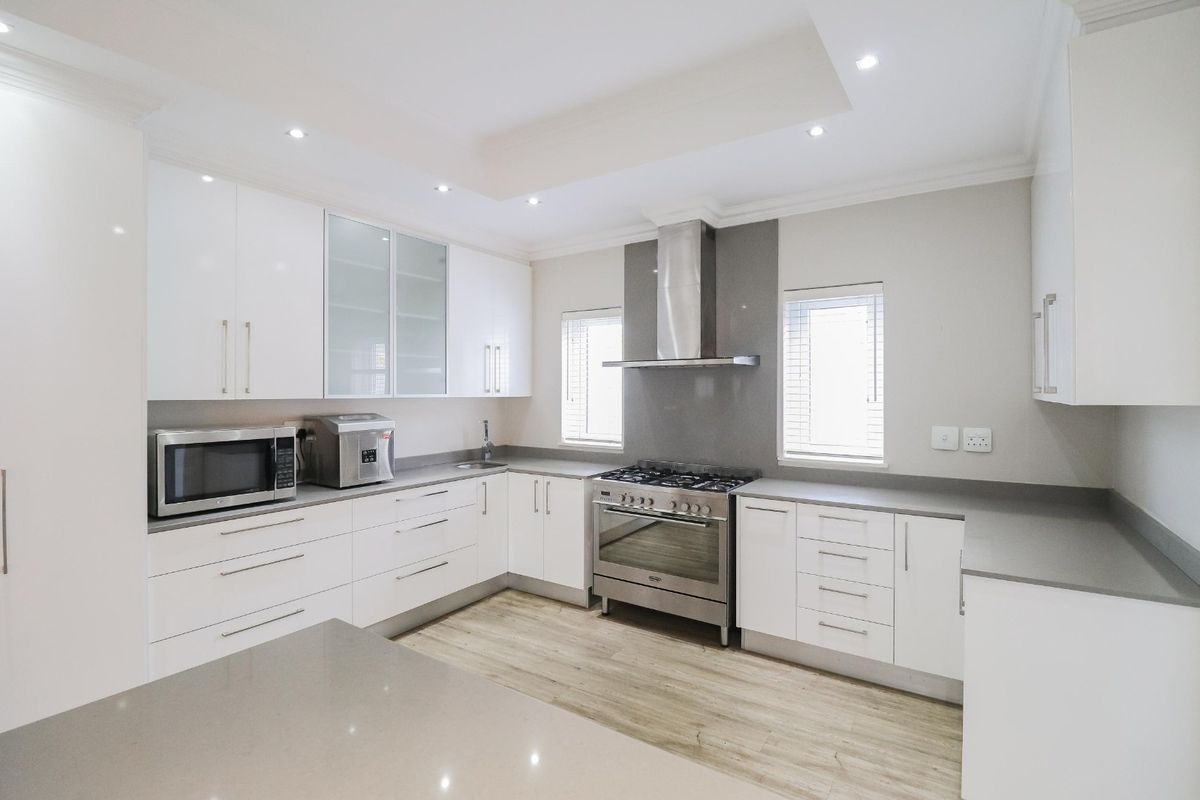 Modern kitchen featuring white cabinetry, stone countertops, stainless steel gas stove, extractor fan, and recessed lighting with a clean, contemporary finish.