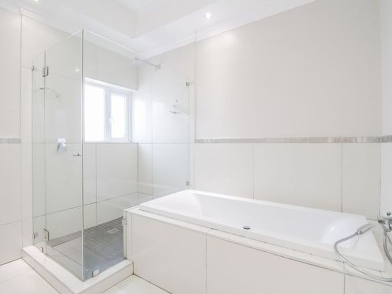 Modern bathroom featuring a glass-enclosed shower, a built-in bathtub, and clean white tiled finishes throughout.