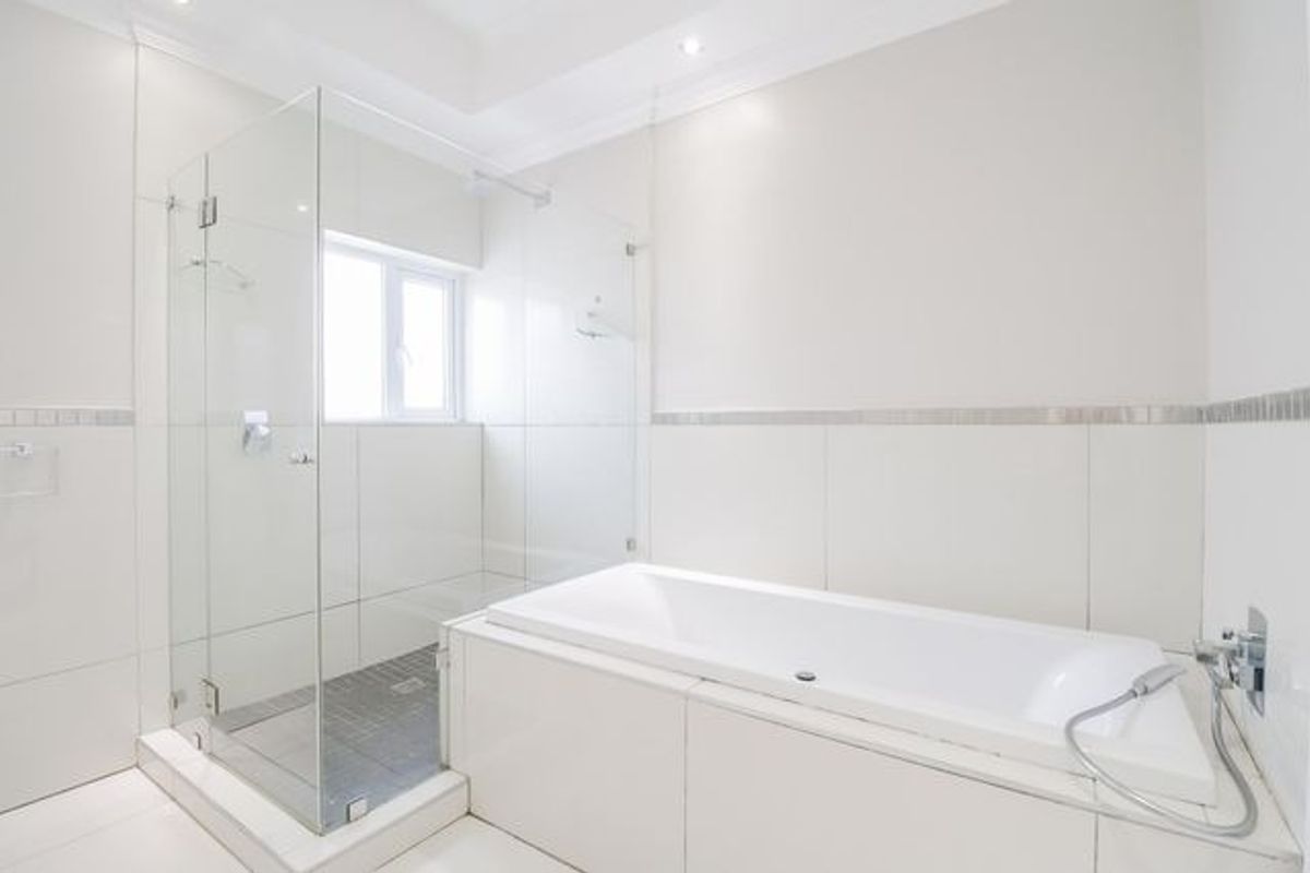 Modern bathroom featuring a glass-enclosed shower, a built-in bathtub, and clean white tiled finishes throughout.