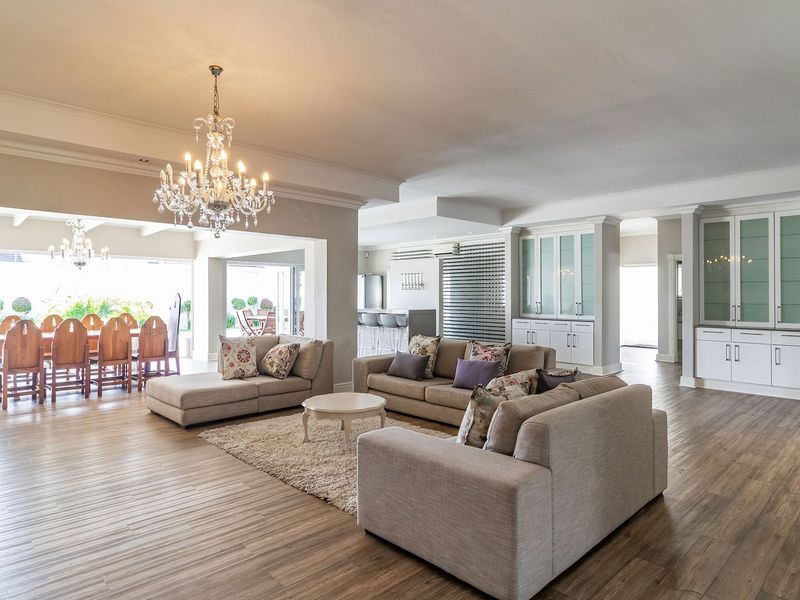 Spacious open-plan living and dining area featuring wood-look flooring, elegant chandeliers, and extensive built-in cabinetry, seamlessly connecting to the outdoor patio.