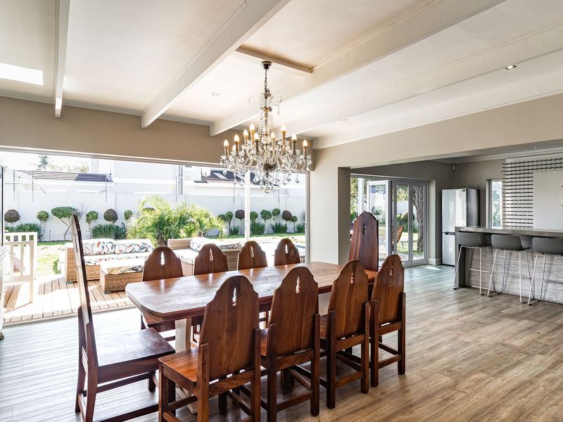 Spacious open-plan dining and bar area featuring exposed ceiling beams, a crystal chandelier, and large bi-fold doors opening to an outdoor patio.