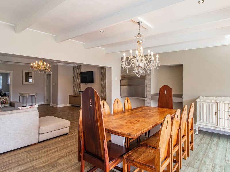Spacious open-plan living and dining area featuring exposed ceiling beams, laminate flooring, a built-in indoor braai, and elegant crystal chandeliers.
