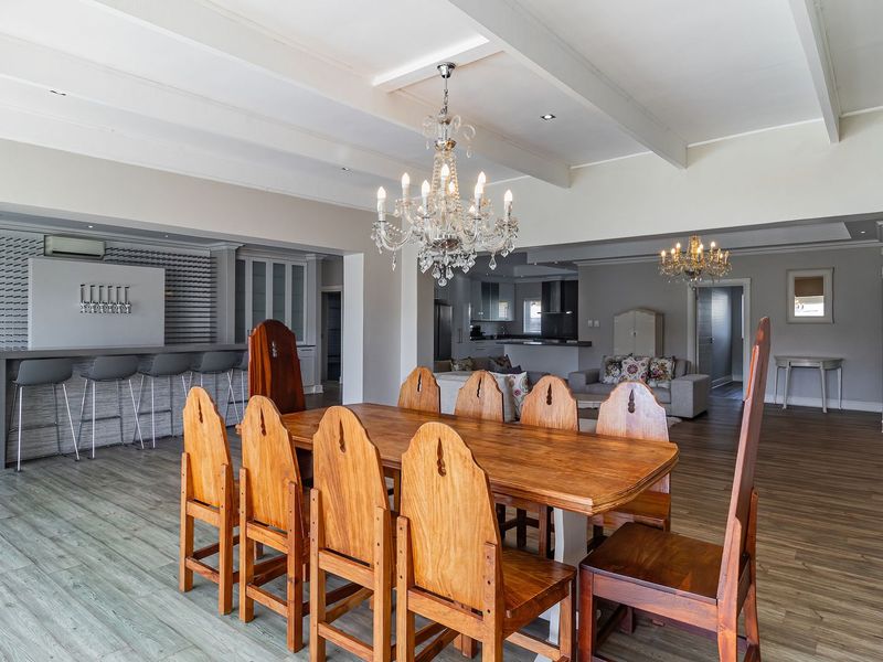 Spacious open-plan living and dining area featuring exposed ceiling beams, a built-in bar, and elegant chandelier lighting with modern laminate flooring throughout.