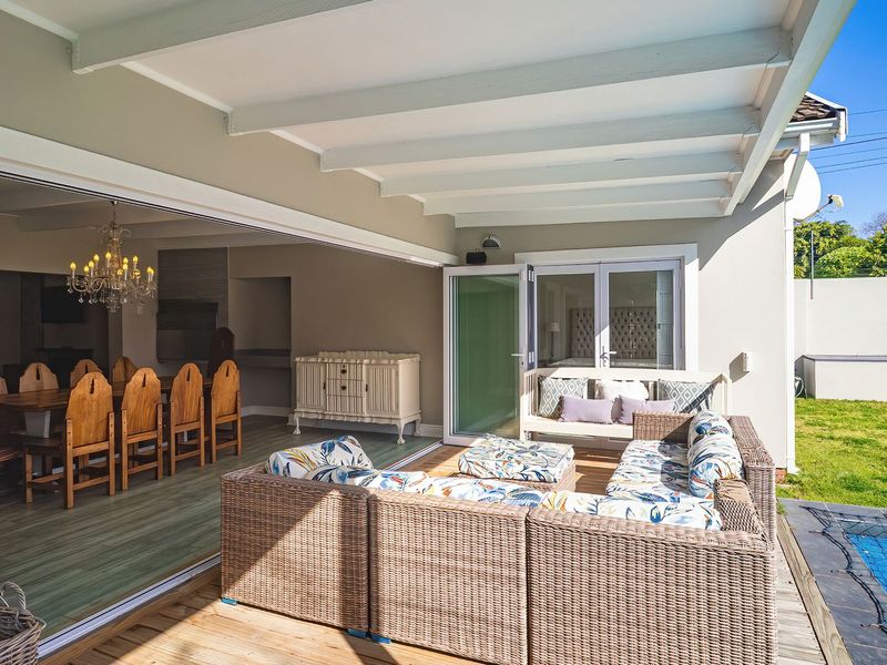 Spacious covered patio featuring wooden decking, seamless indoor-outdoor flow through sliding doors, and direct access to the swimming pool and garden area.