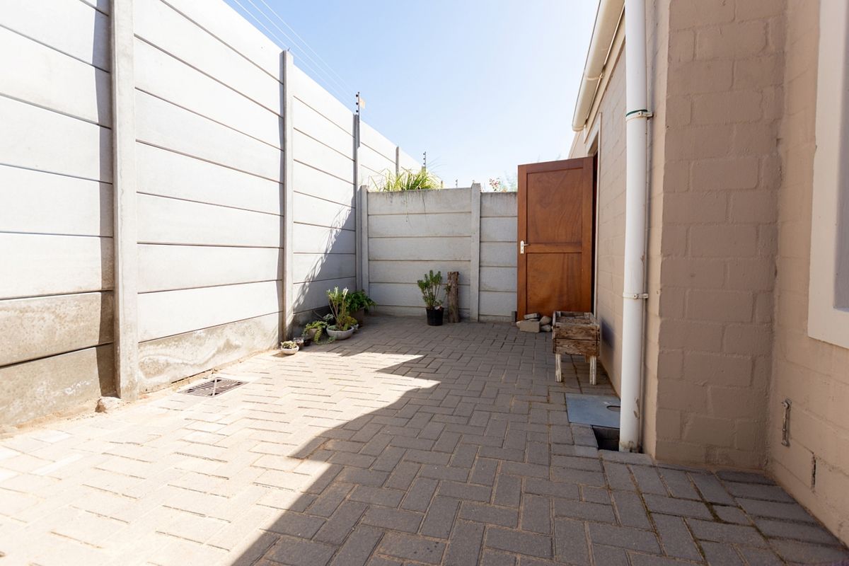 A private rear courtyard featuring paved flooring, enclosed by precast concrete boundary walls with a side access door.