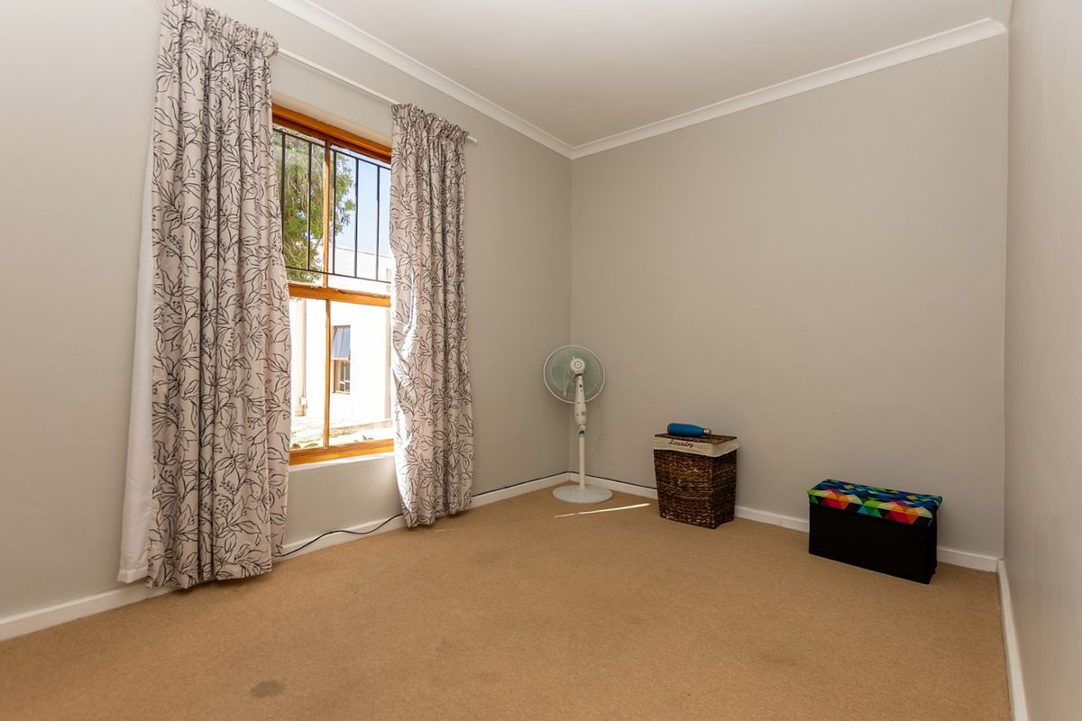 A neutral, carpeted bedroom featuring a window with security bars and coving, offering a blank canvas for personalization.