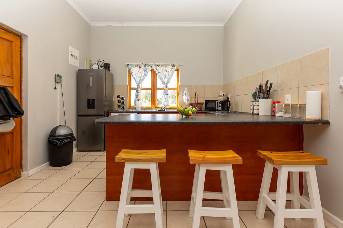 A functional kitchen featuring a central island with breakfast bar seating, tiled backsplash, and neutral floor tiles.