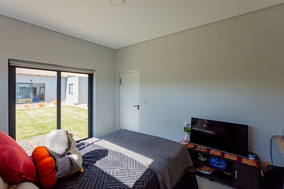 A modern bedroom featuring neutral walls, a sliding glass door providing access to the garden, and a clean, minimalist interior finish.