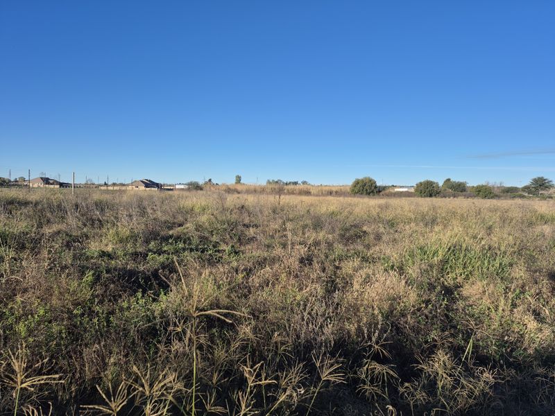 An expansive, undeveloped plot of land featuring natural wild grass and distant perimeter fencing, offering significant potential for future development.