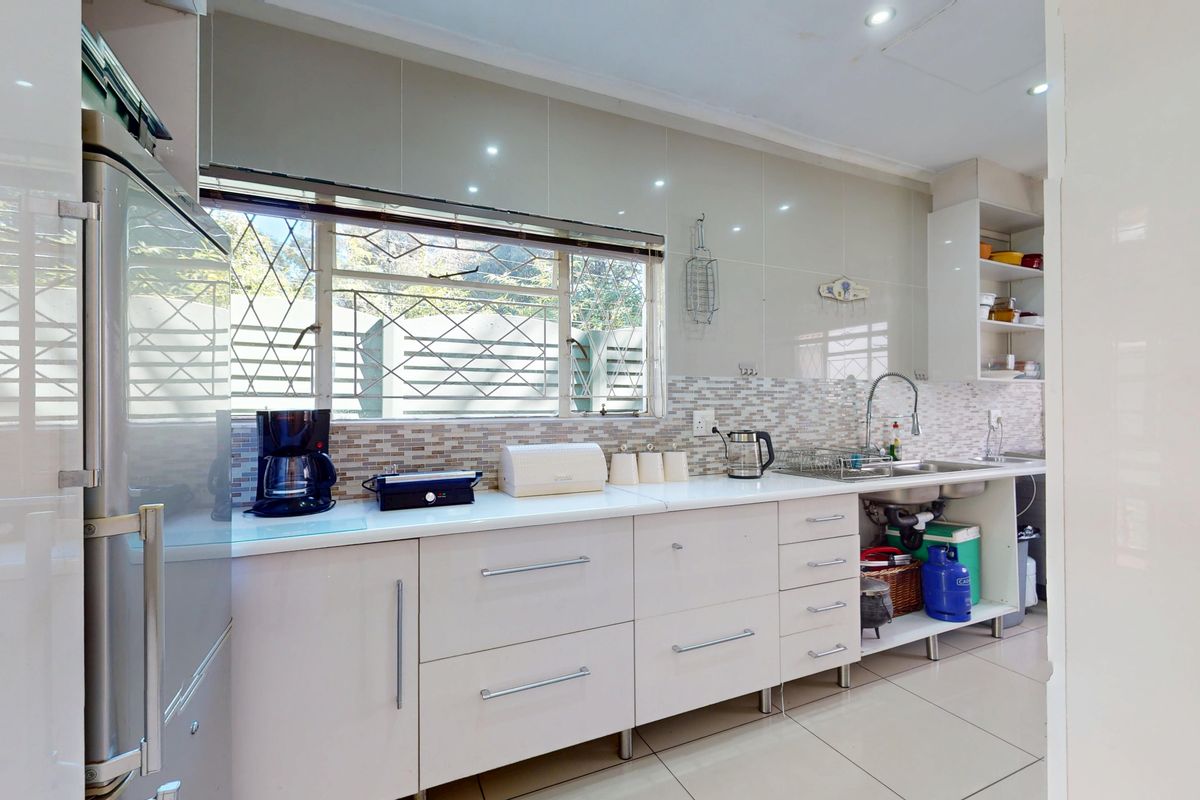 A functional kitchen featuring modern white cabinetry, a double basin sink, tiled backsplash, and large windows with security bars.