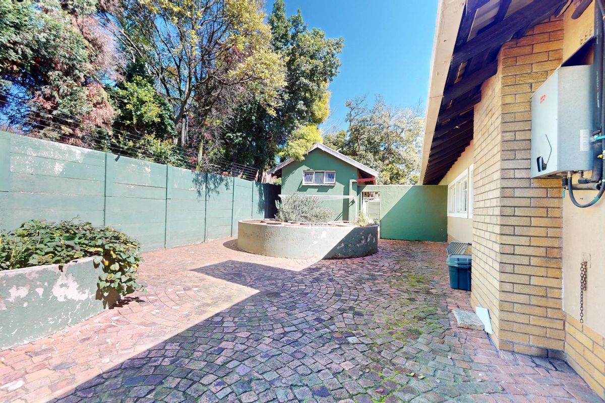 A rear courtyard area featuring brick paving, raised garden beds, and a brick exterior wall with an installed gas geyser.