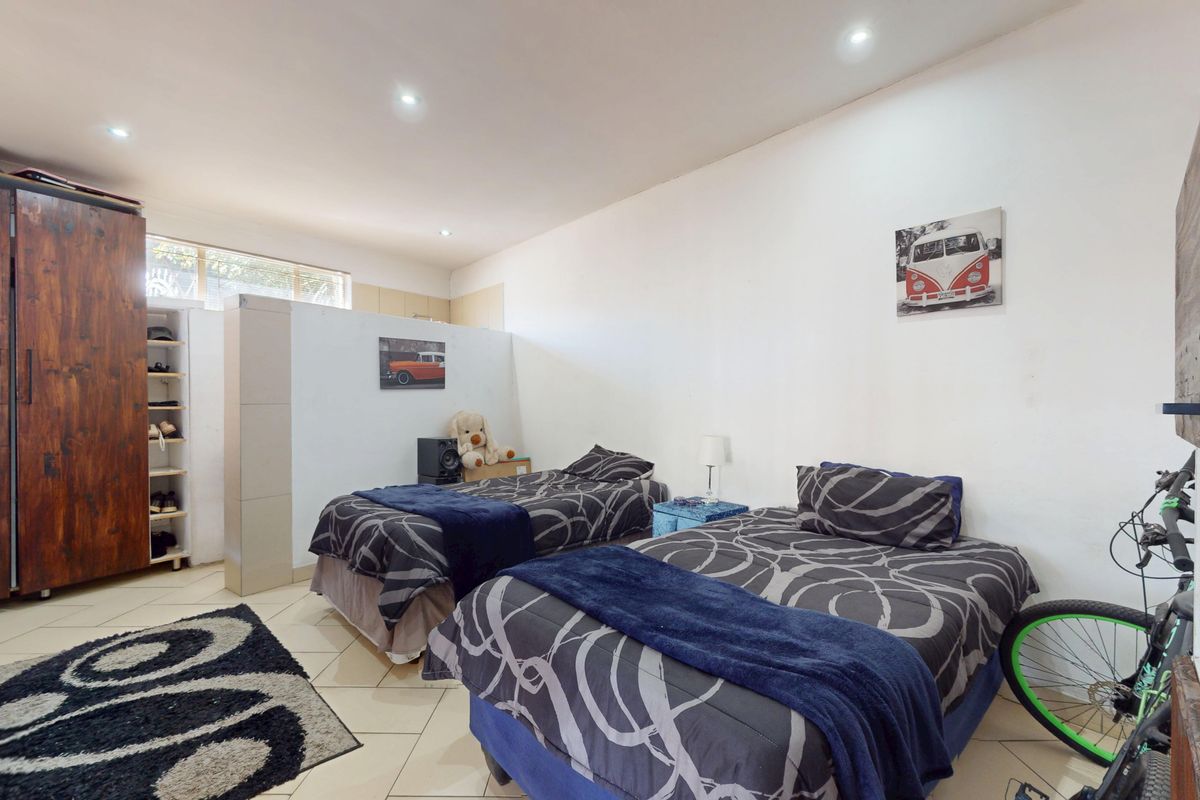 A spacious bedroom featuring tiled flooring, recessed downlighting, and a partial room divider, offering a functional layout with neutral wall finishes.