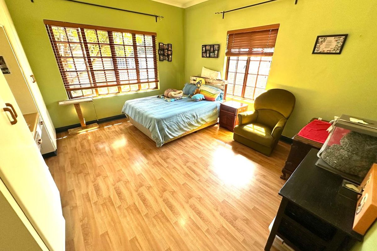 Spacious bedroom featuring laminate flooring, built-in cupboards, and large windows with wooden blinds, offering a bright and functional living space.