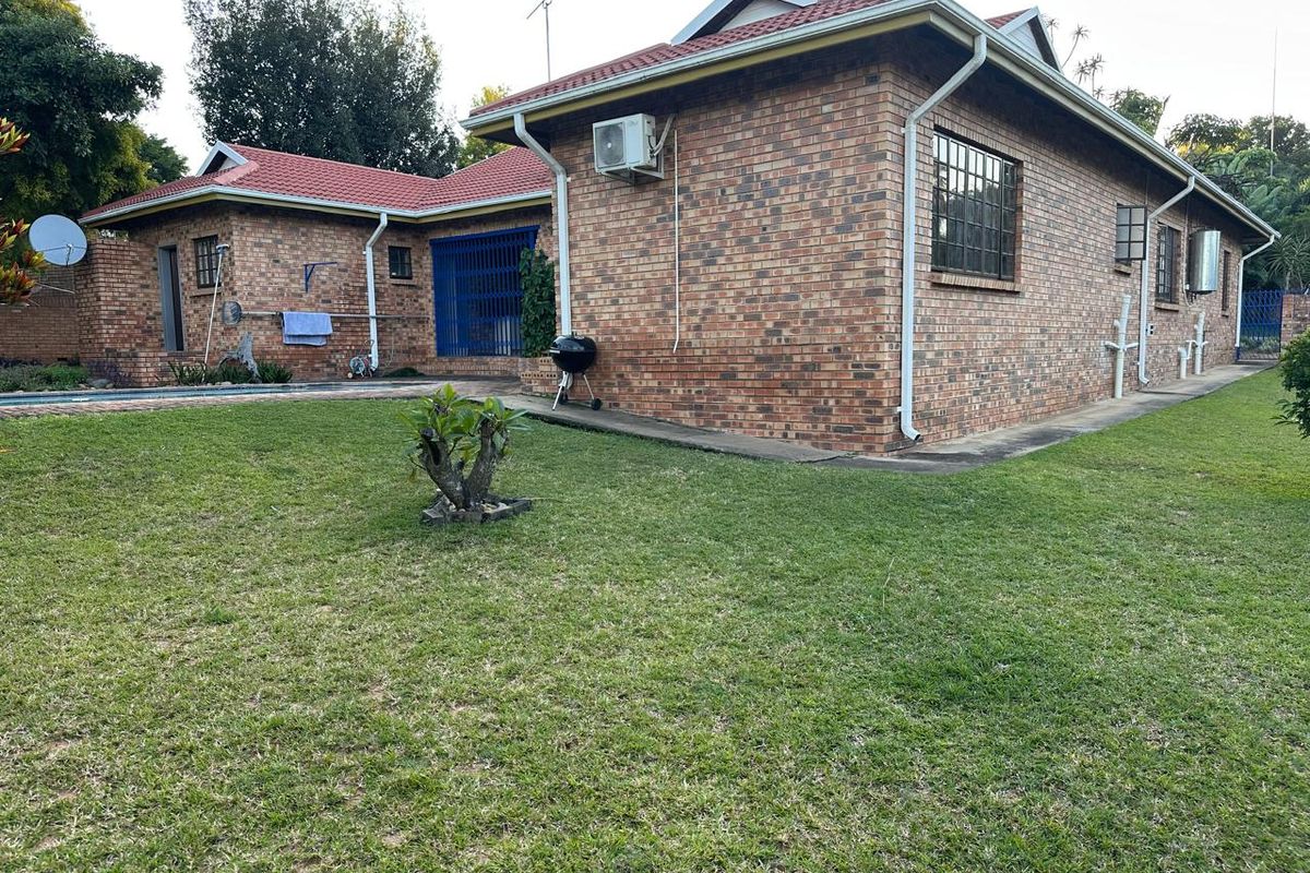 Rear view of the brick house featuring a tiled roof, security bars on windows, and an expansive lawn area.