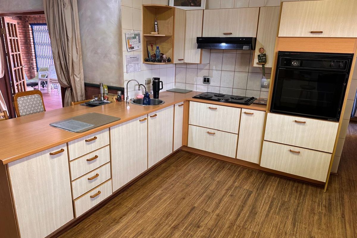 A functional kitchen featuring laminate cabinetry, built-in oven, electric hob, extractor fan, and wood-look flooring, offering a practical layout for daily meal preparation.