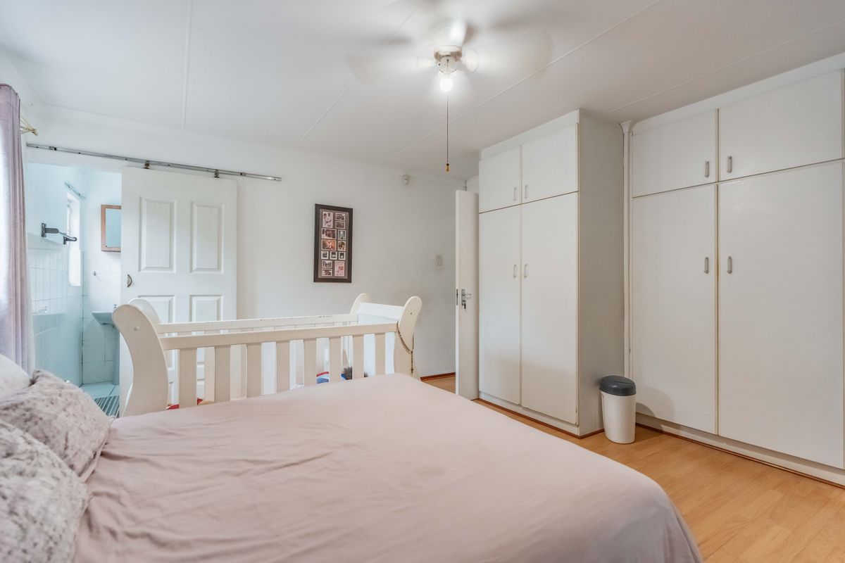 A bedroom featuring built-in cupboards, laminate flooring, and a ceiling fan, with an adjoining en-suite bathroom accessible via a sliding door.