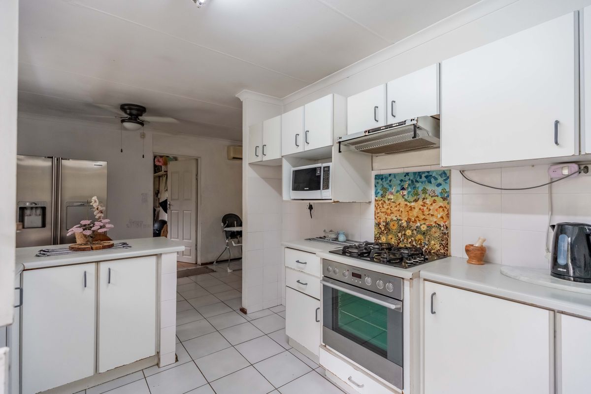 Functional kitchen featuring white cabinetry, gas hob, built-in oven, extractor fan, and tiled flooring with a decorative splashback.