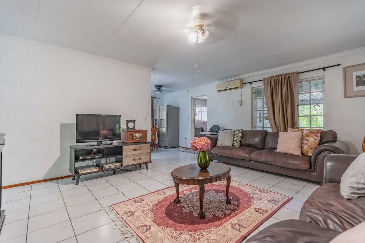 Spacious living room featuring tiled flooring, a ceiling fan, and a wall-mounted air conditioning unit, with an open-plan flow toward the kitchen area.