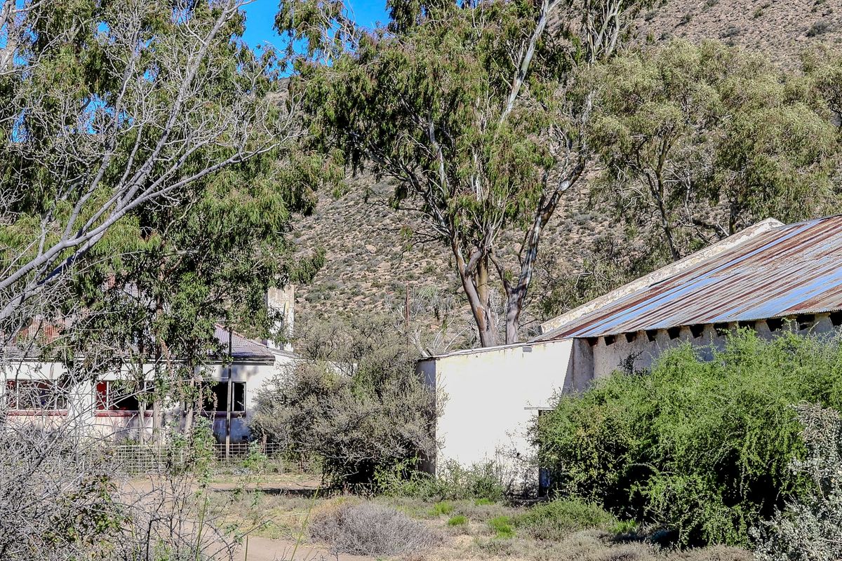Exterior view of a rural farm property featuring weathered masonry structures with rusted corrugated metal roofing set against a hillside.