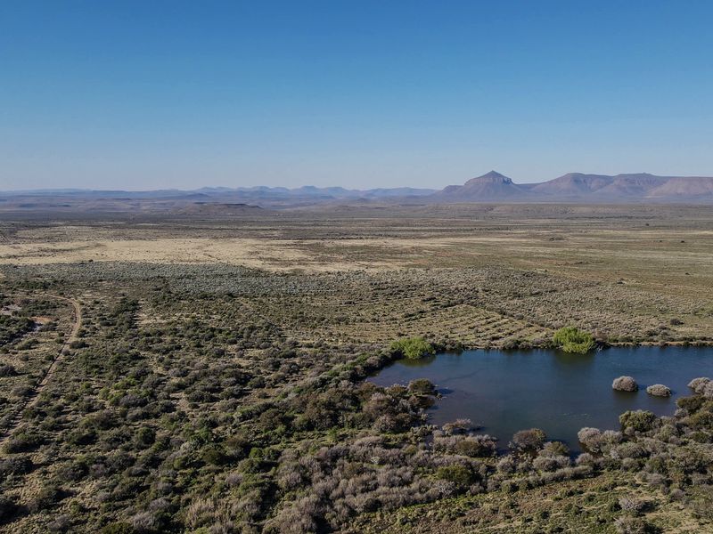 An aerial view of the expansive farm landscape featuring a natural dam and surrounding indigenous vegetation under a clear blue sky.