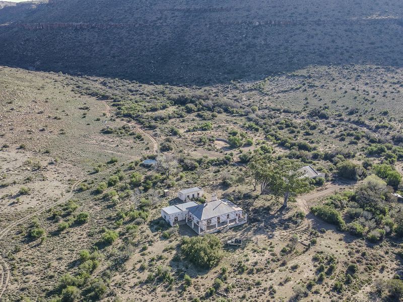 Aerial view of a rural farm property featuring a main farmhouse, outbuildings, and surrounding natural landscape with a dirt access road.