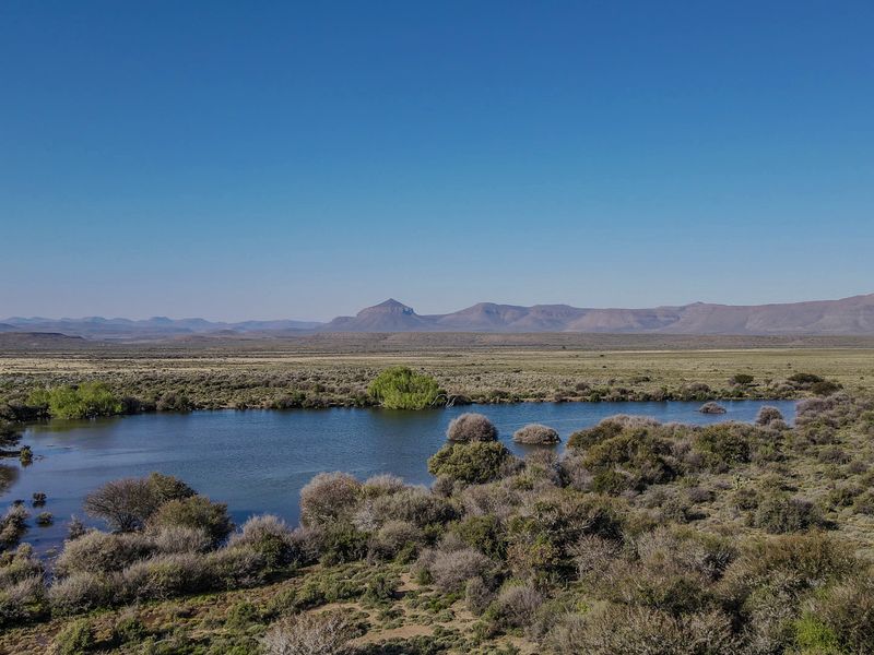 A scenic landscape view featuring a natural dam surrounded by indigenous vegetation with a mountain range in the background.