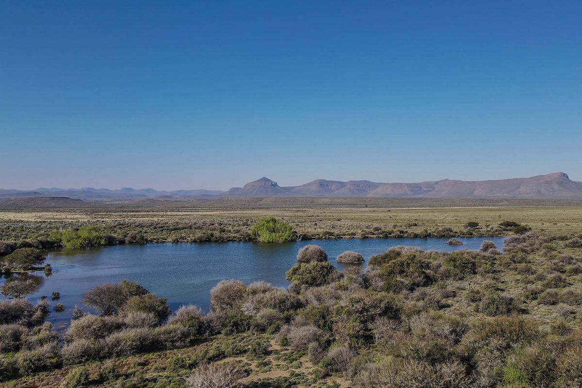 A scenic landscape view featuring a natural dam surrounded by indigenous vegetation with a mountain range in the background.