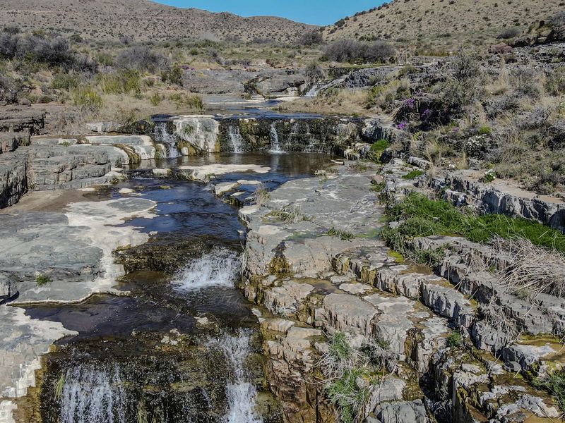 A scenic view of a natural stream flowing over rocky terrain and small waterfalls within the farm landscape.