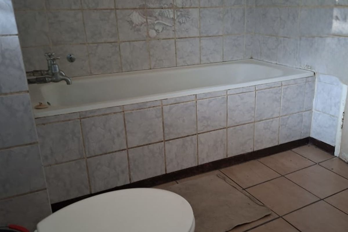 A dated bathroom featuring a built-in bathtub with ceramic wall and floor tiling, requiring cosmetic updates to modernize the space.