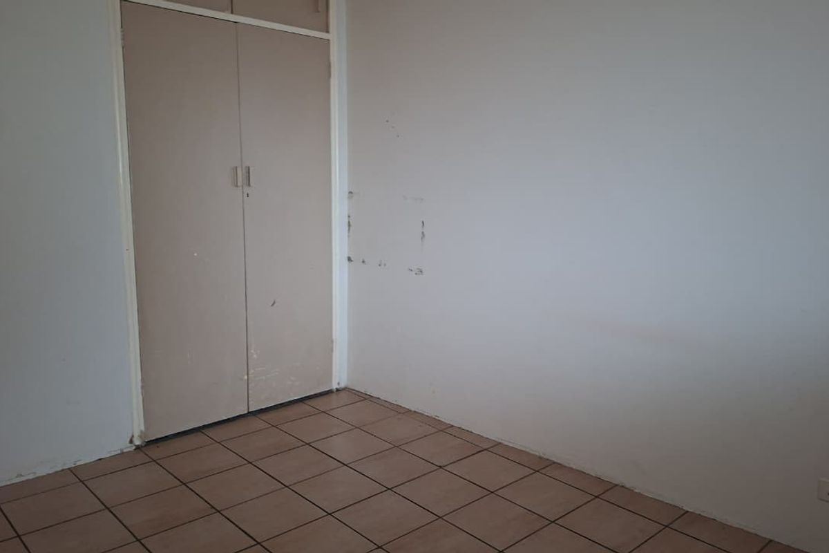 An empty bedroom featuring tiled flooring and built-in cupboards, requiring minor cosmetic updates to the walls and cabinetry.