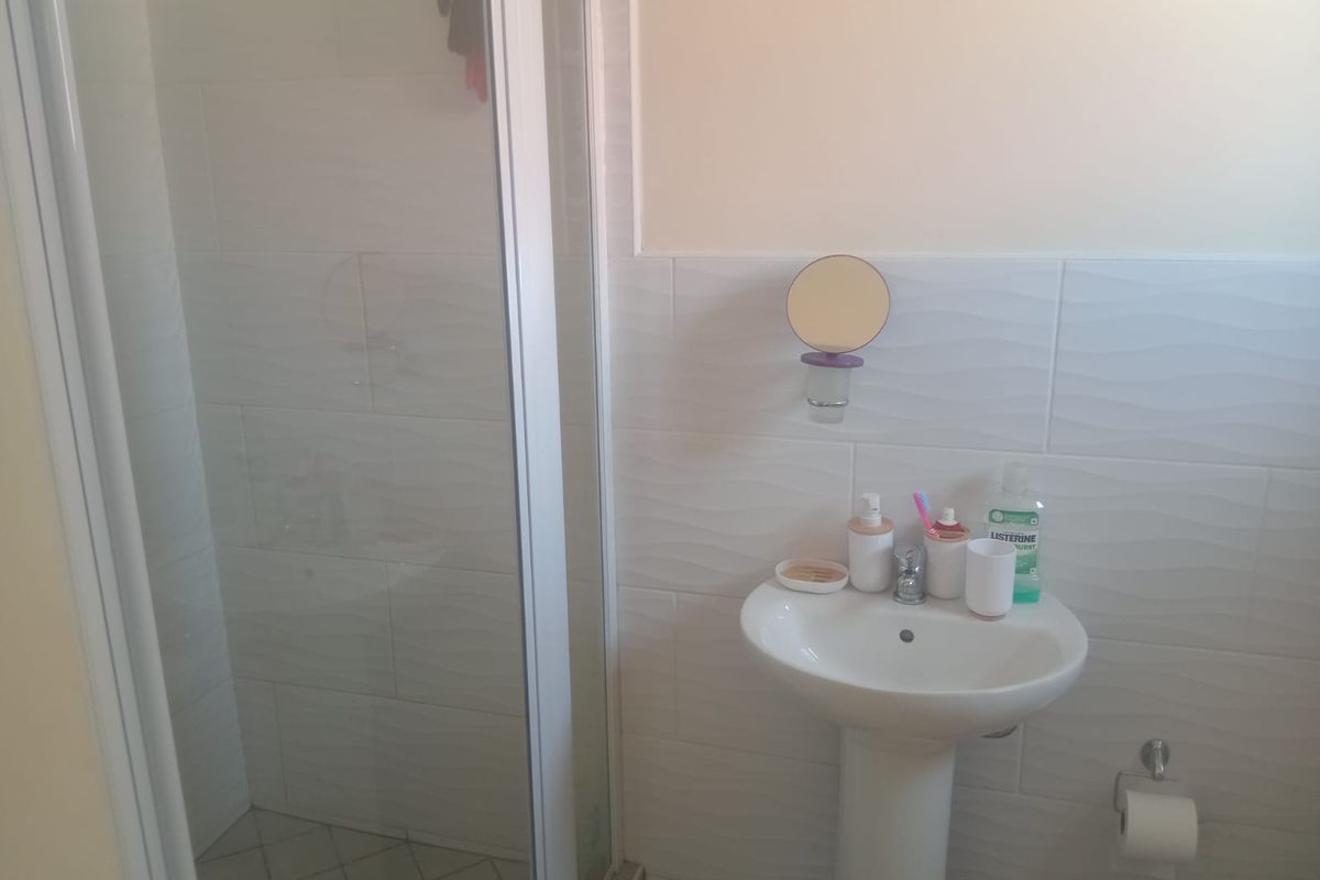 A functional bathroom featuring a pedestal basin and a glass-enclosed shower with textured wall tiling.