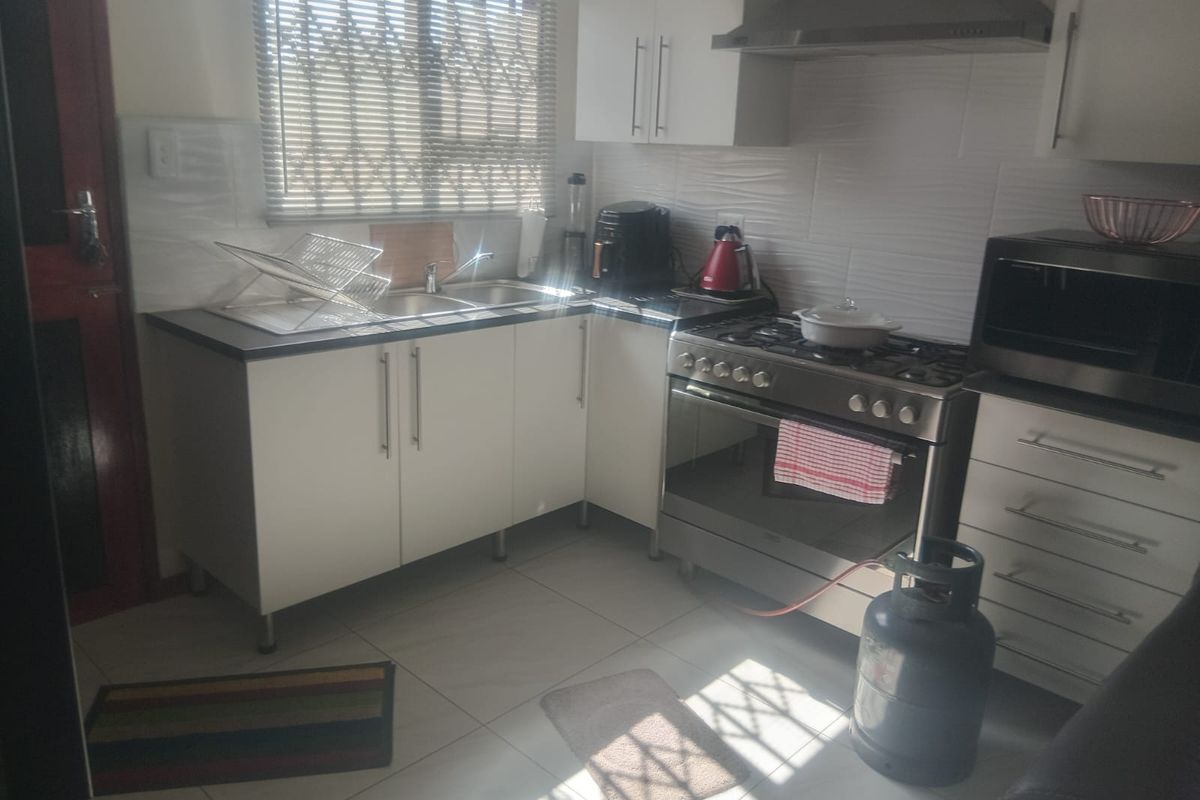 A functional kitchen featuring white cabinetry, a gas stove with extractor fan, stainless steel sink, and tiled flooring with natural light.