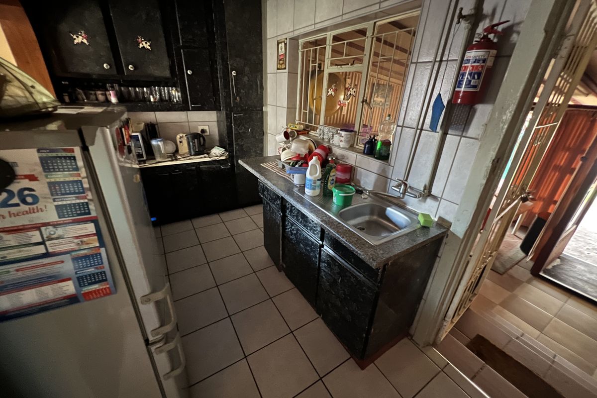 A compact kitchen featuring dark built-in cabinetry, tiled flooring, and a stainless steel sink with a window overlooking the exterior.