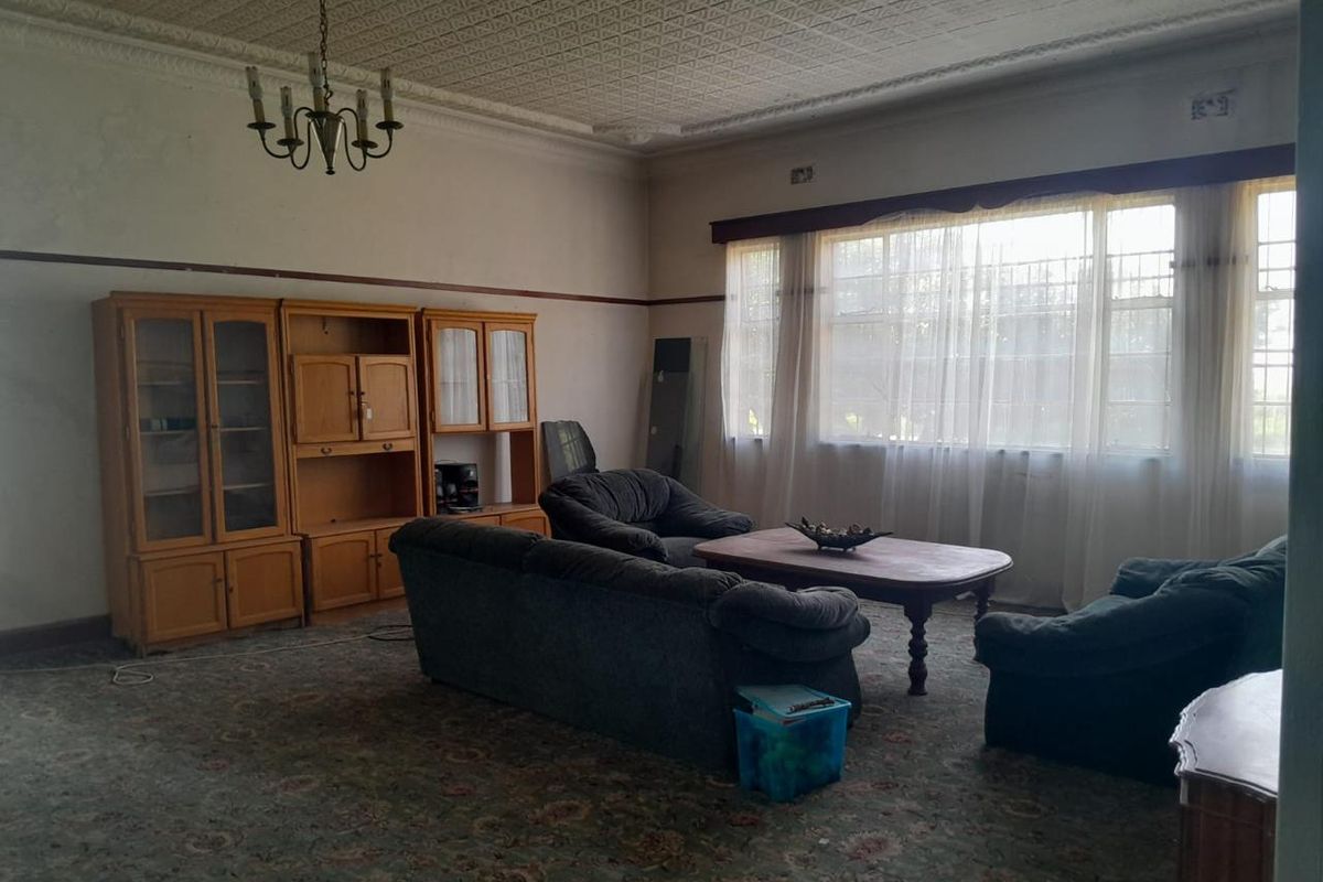 Spacious living room featuring a classic ornate pressed metal ceiling, large windows with security bars, and a built-in wooden wall unit.