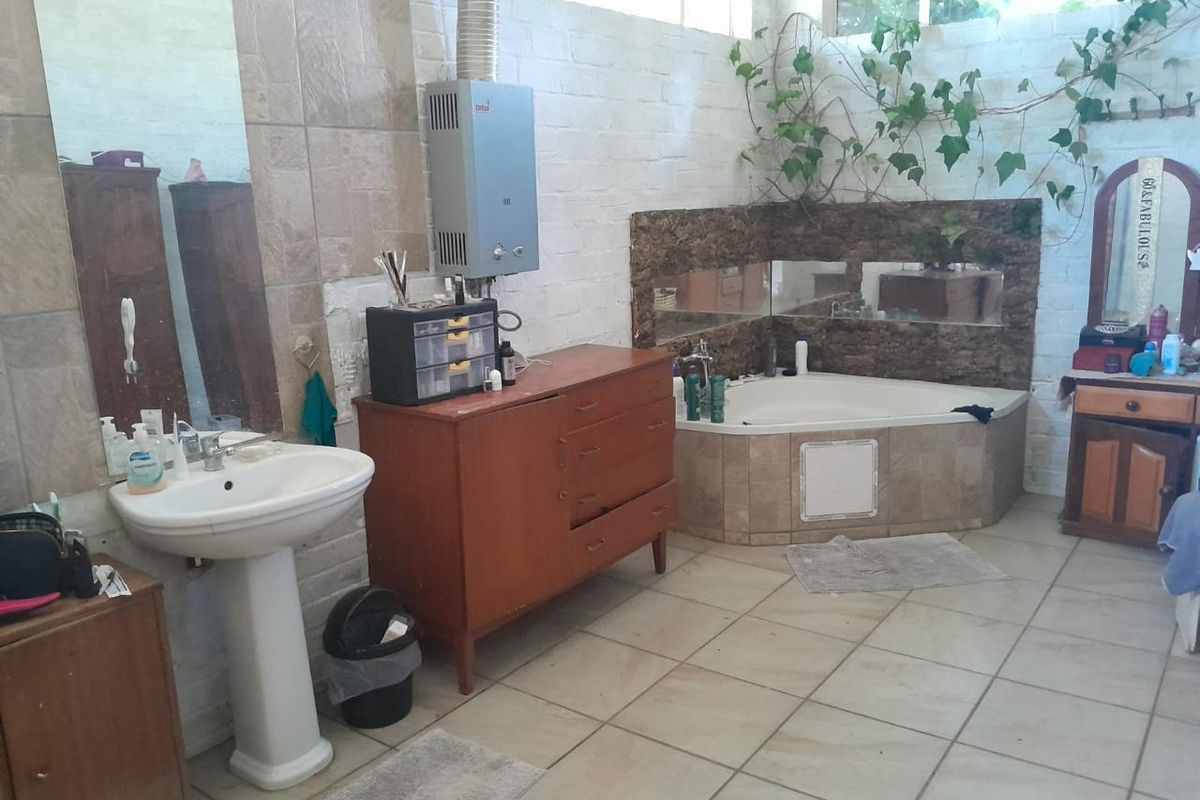 Spacious bathroom featuring a corner bathtub, pedestal basin, and wall-mounted gas geyser, with tiled flooring and partially finished brick walls.