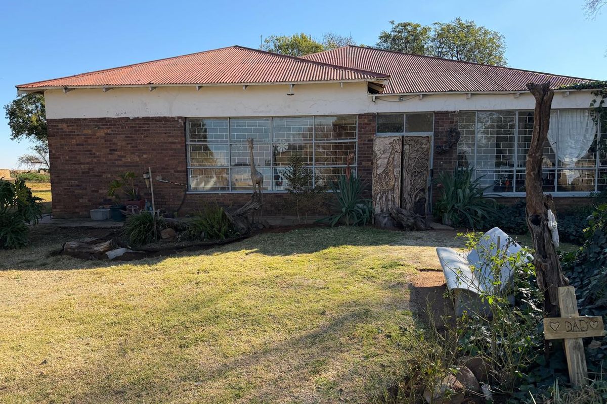 Rear view of a brick small holding dwelling featuring a corrugated metal roof and large windows with security bars.