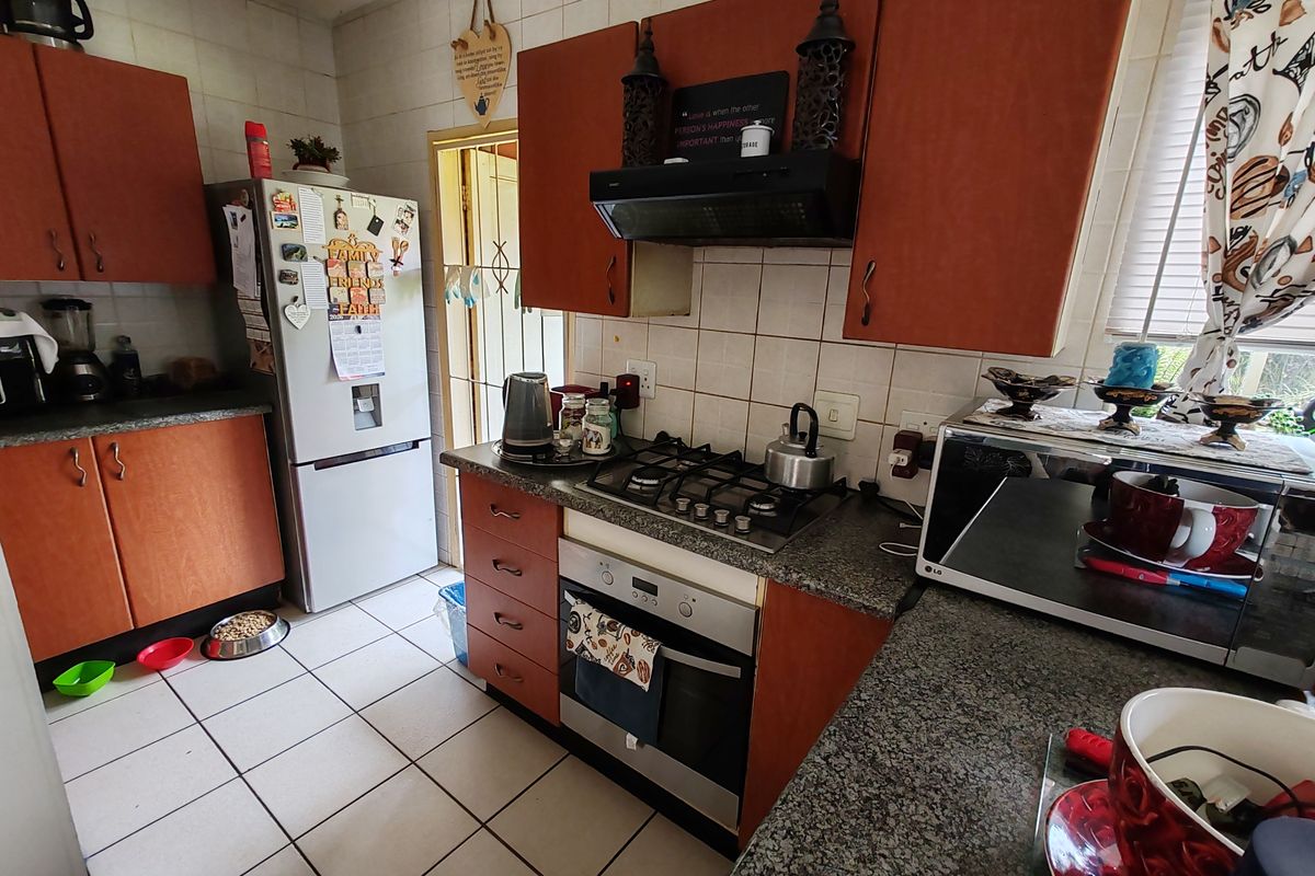 A functional kitchen featuring wooden cabinetry, granite countertops, a gas hob, and a built-in oven with a tiled backsplash and flooring.
