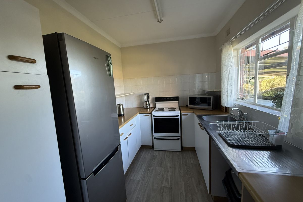 A functional kitchen featuring white cabinetry, laminate countertops, a tiled splashback, and a freestanding stove, offering a practical layout for daily meal preparation.