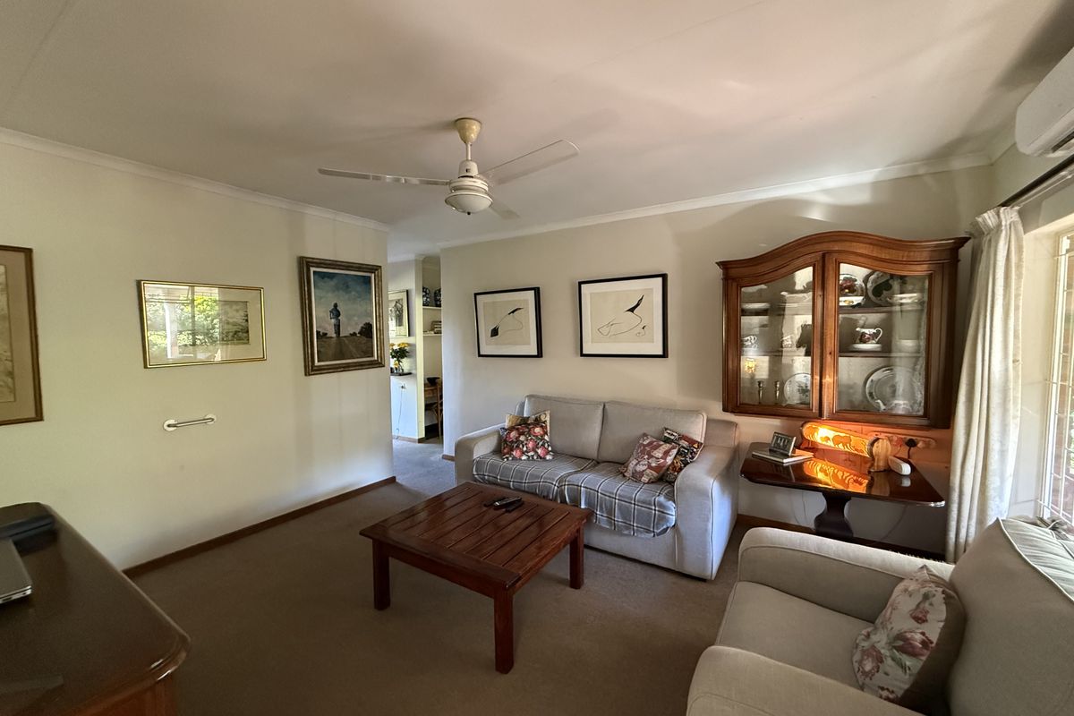 A comfortable living room featuring carpeted flooring, a ceiling fan, and a wall-mounted air conditioning unit.
