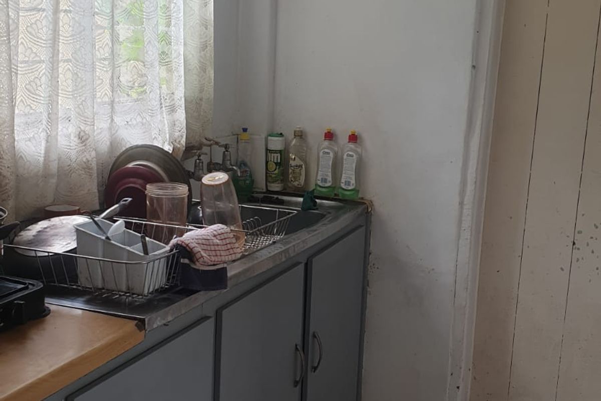 A compact kitchen area featuring grey cabinetry, a stainless steel sink, and tiled flooring, offering a functional space with potential for modernization.