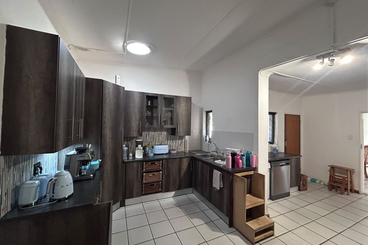 A functional kitchen featuring dark wood cabinetry, tiled flooring, and a tiled backsplash, with an adjacent area suitable for additional storage or appliances.