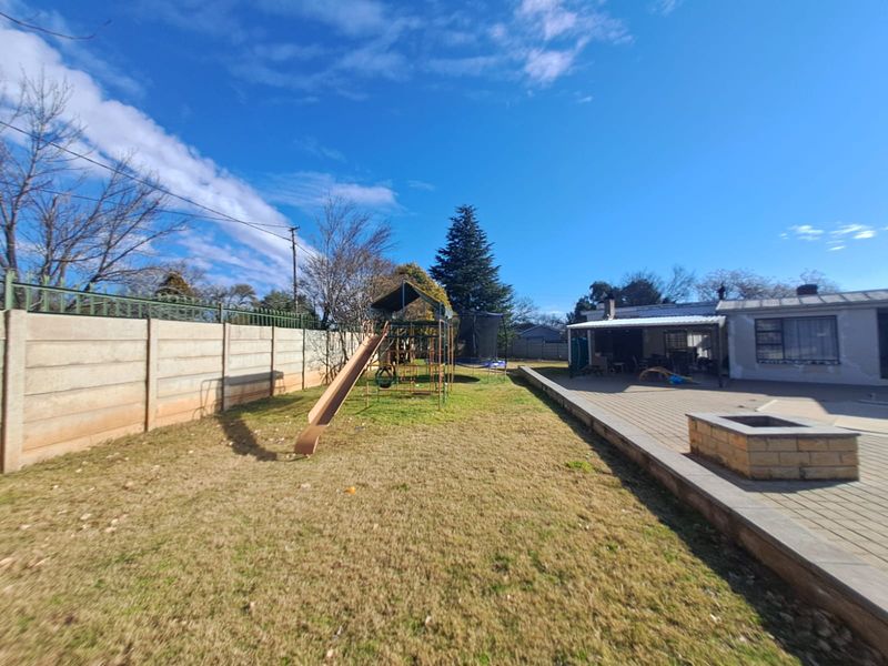 Spacious rear garden featuring a paved patio area with a built-in fire pit, covered patio space, and a precast concrete boundary wall.