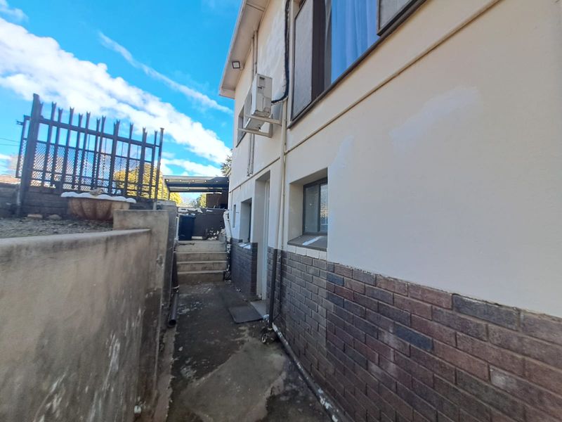 Side exterior view of the property featuring a brick and plaster facade, concrete pathway, and mounted air conditioning unit.
