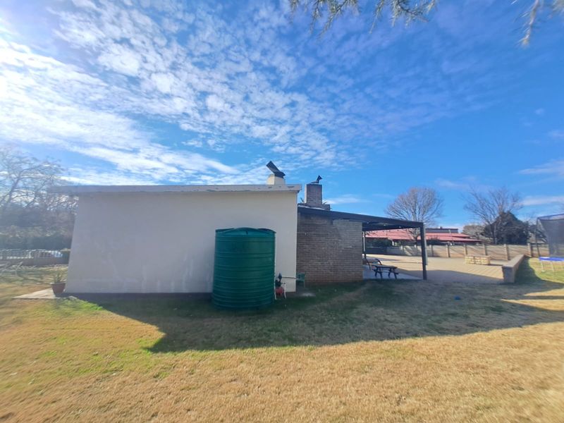 Rear view of the property featuring a covered patio, brick chimney, and a large water storage tank set within a spacious garden area.